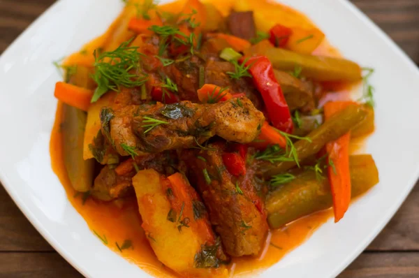 Stufato con patate, carote, sottaceti, pomodori e peperoncini. Azu di tartaro su un piatto quadrato bianco. Sfondo rustico in legno. Vista dall'alto. Primo piano — Foto Stock