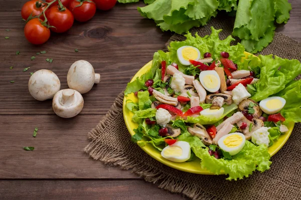 Salată cu ciuperci, pui, ouă de prepeliță, ardei, salată verde și rodie, pe o masă de lemn. Privire de sus — Fotografie, imagine de stoc