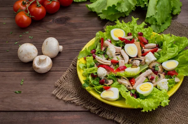 Salada com cogumelos, frango, ovos de codorna, páprica, alface e romã, em uma mesa de madeira. Vista superior — Fotografia de Stock