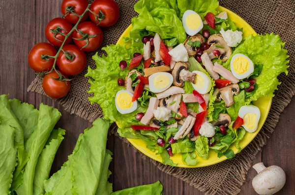 Salada com cogumelos, frango, ovos de codorna, páprica, alface e romã, em uma mesa de madeira. Vista superior — Fotografia de Stock