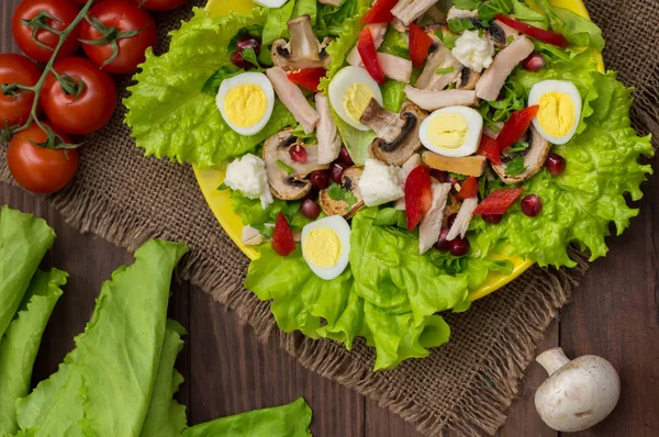 Salade met champignons, kip, kwarteleitjes, paprika, sla en granaatappel, op een houten tafel. Bovenaanzicht — Stockfoto