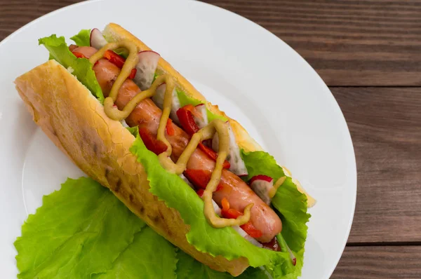 Hot Dog mit Grillwurst, Salat, Rettich und Senf, auf einem hölzernen Hintergrund. Ansicht von oben — Stockfoto