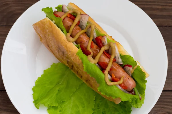 Hot Dog mit Grillwurst, Salat, Rettich und Senf, auf einem hölzernen Hintergrund. Ansicht von oben — Stockfoto