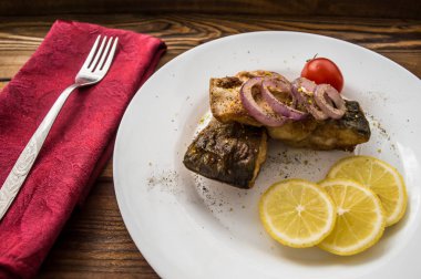 Kızarmış balık fileto limon ve beyaz tabakta domates. Ahşap arka plan. Üstten Görünüm. Yakın çekim