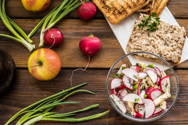 Salat mit Radieschen, Äpfeln, Gemüse und einer Sandwich-Fischpastete. Holzuntergrund. Ansicht von oben. Nahaufnahme — Stockfoto