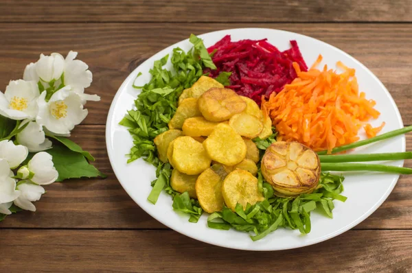 Plat avec pommes de terre frites, betteraves, carottes et laitue sur fond de fleurs. Table en bois. Gros plan — Photo