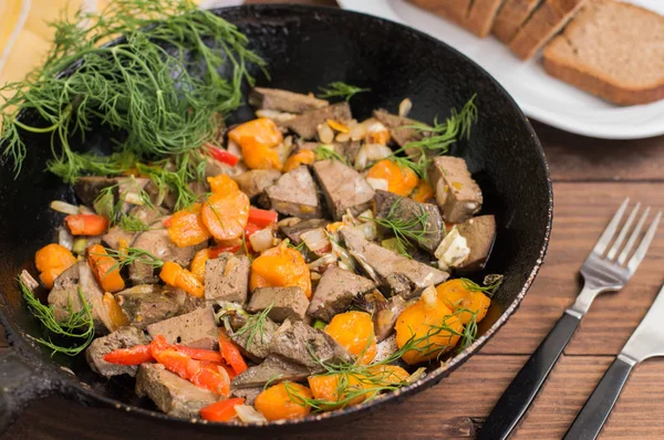 Braised liver with onions, carrots, potatoes and spices on stone plate. Wooden background. Top view. Close-up