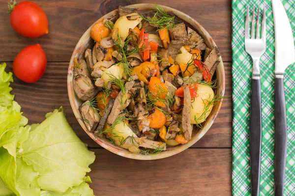 Fegato brasato con cipolle, carote, patate e spezie sul piatto di pietra. Sfondo in legno. Vista dall'alto. Primo piano — Foto Stock