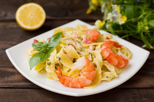 Fettuccine pasta in cream sauce with king prawns on a plate  the wooden table. Horizontal view from above. Top . Close-up