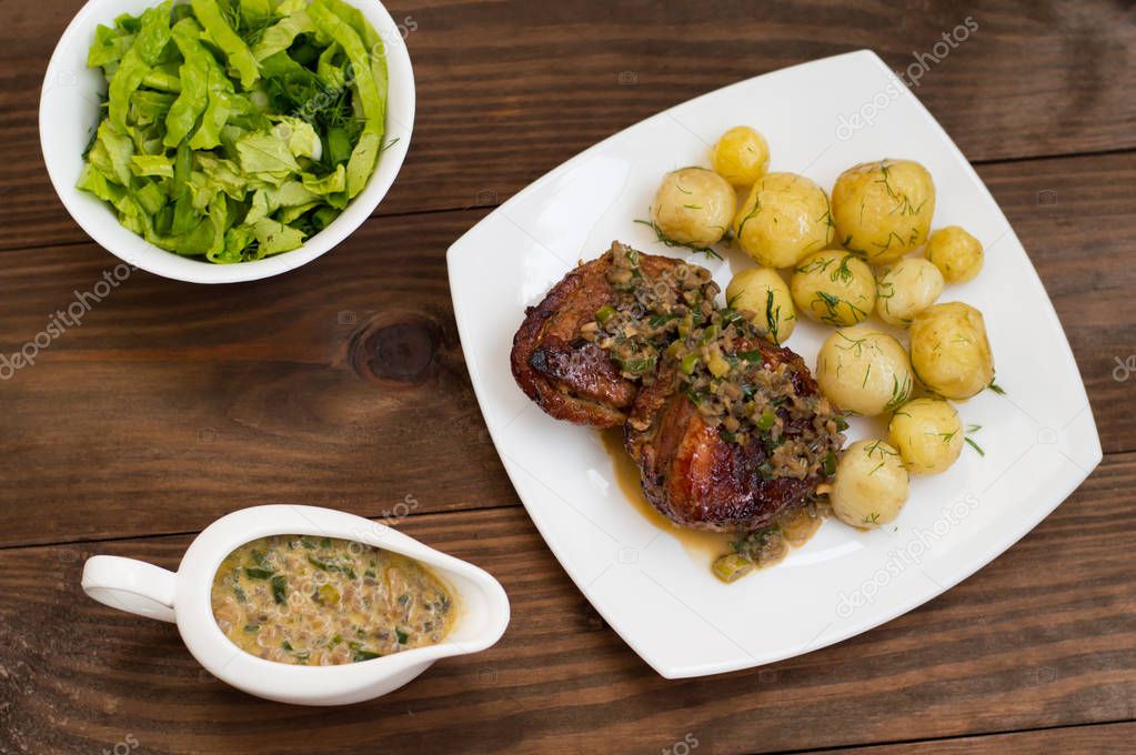 Pork medallions in mushroom sauce with new potatoes. Restaurant supply. Wooden table. Top view. Close-up