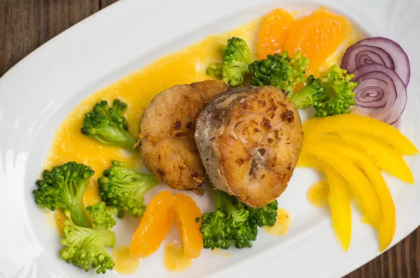 Deliciosos filetes de pescado asado en la sartén. Publicado con salsa de mandarina, pimienta y rebanadas de brócoli hervido al dente. Fondo de madera. Vista superior. Primer plano —  Fotos de Stock