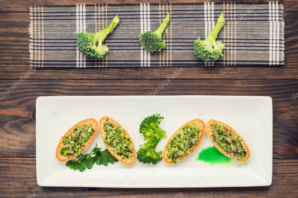 Tartlets stuffed with minced meat  broccoli and tuna. Wooden background