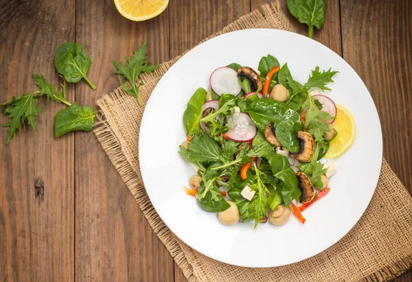 Insalata di primavera fresca con ravanello, Mizuno, funghi alla griglia, formaggio Adygei, spinaci, peperone, limone, mais. Sfondo in legno — Foto Stock