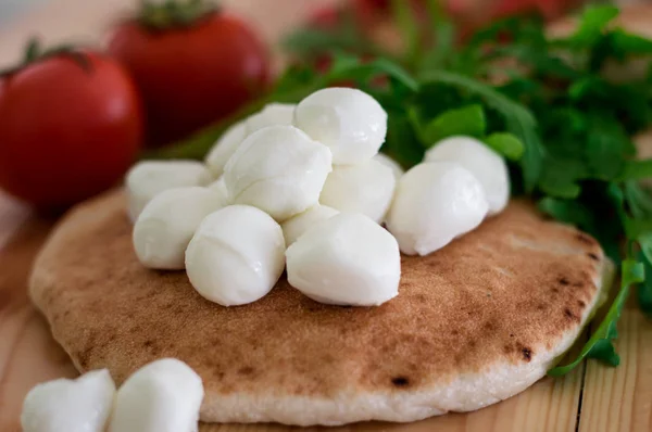 Pita bread with mozzarella, greens and tomatoes. Israeli national pastries on wooden background. Close-up. Top view