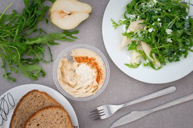 Humus ve yeşil roka bitki, armut ve izole peynir salatası. Rustik tarzı. Gri taş arka plan. Üstten Görünüm. Yakın çekim
