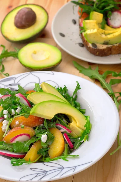 Zeleninový salát s avokádem, rukolou, ředkvičkami a broskev. Dietní zdravé jídlo. Dřevěné pozadí. Pohled shora. Detail — Stock fotografie