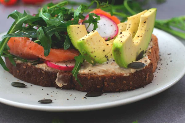 Zelfgemaakte sandwich met avocado, zalm, rucola en humus. Rustieke stijl. Grijze stenen achtergrond. Close-up. Bovenaanzicht — Stockfoto