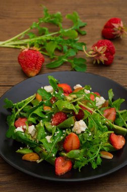 Roka, çilek, süzme peynir, zeytinyağı, ahşap arka plan siyah bir tabakta salatası. Yakın çekim. Üstten Görünüm