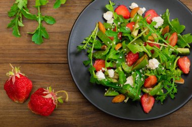 Roka, çilek, süzme peynir, zeytinyağı, ahşap arka plan siyah bir tabakta salatası. Yakın çekim. Üstten Görünüm