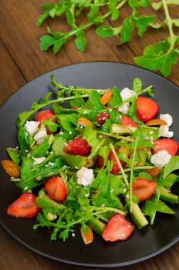 Roka, çilek, süzme peynir, zeytinyağı, ahşap arka plan siyah bir tabakta salatası. Yakın çekim. Üstten Görünüm