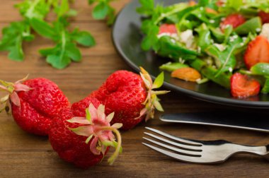 Roka, çilek, süzme peynir, zeytinyağı, ahşap arka plan siyah bir tabakta salatası. Yakın çekim. Üstten Görünüm