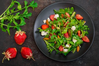Roka, çilek, süzme peynir, zeytinyağı, eski siyah arka plan siyah bir tabakta salatası. Yakın çekim. Üstten Görünüm