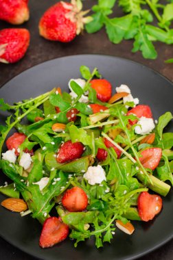 Roka, çilek, süzme peynir, zeytinyağı, eski siyah arka plan siyah bir tabakta salatası. Yakın çekim. Üstten Görünüm