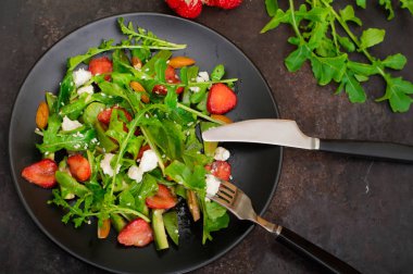 Roka, çilek, süzme peynir, zeytinyağı, eski siyah arka plan siyah bir tabakta salatası. Yakın çekim. Üstten Görünüm