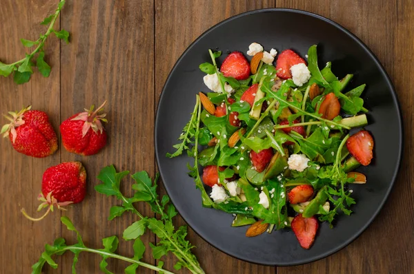 Arugula, 딸기, 코 티 지 치즈, 검은 접시, 나무 배경에 올리브 오일, 샐러드. 클로즈업입니다. 상위 뷰 — 스톡 사진