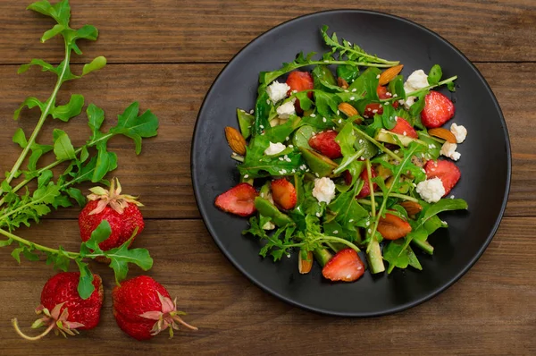 Roka, çilek, süzme peynir, zeytinyağı, ahşap arka plan siyah bir tabakta salatası. Yakın çekim. Üstten Görünüm — Stok fotoğraf