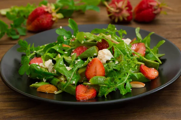 Salad dengan arugula, stroberi, keju cottage, minyak zaitun, di piring hitam, latar belakang kayu. Close-up. Tampilan atas — Stok Foto