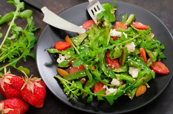 Salada com arugula, morangos, queijo cottage, azeite, em um prato preto, fundo preto velho. Close-up. Vista superior — Fotografia de Stock