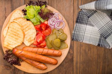 Gıda koymak sosis, sucuk, konserve salatalık, marul yaprakları, domates, soğan, kruton ahşap arka plan üzerinde. Yakın çekim. Üstten Görünüm