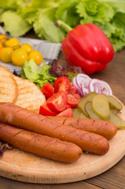 Gıda koymak sosis, sucuk, konserve salatalık, marul yaprakları, domates, soğan, kruton ahşap arka plan üzerinde. Yakın çekim. Üstten Görünüm