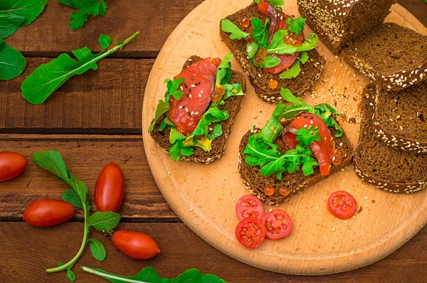 Bruschetta somon balığı, kırmızı balık, kırmızı havyar, roka ve domates bir gemide. Ahşap rustik arka plan. Seçici odak. Üstten Görünüm