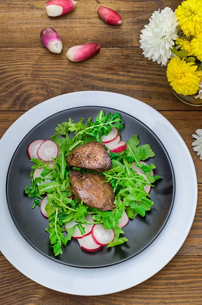 닭 간, arugula, 검은 접시에 소스와 함께 무와 따뜻한 샐러드. 목조 소박한 배경입니다. 선택적 초점입니다. 상위 뷰 — 스톡 사진