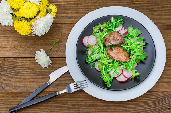 Salade chaude avec foie de poulet, roquette et radis avec sauce sur l'assiette noire. Fond rustique en bois. Concentration sélective. Vue du dessus — Photo
