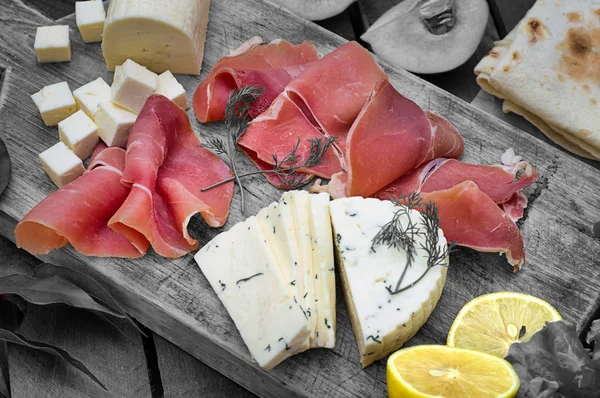 Jamon met verschillende soorten kaas op een houten plank. Houten rustieke achtergrond. Bovenaanzicht — Stockfoto