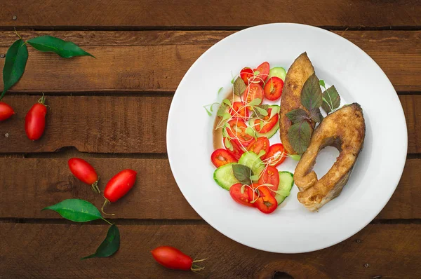 Grilované rybí steak se zeleninou na desce: microgran, rajčata, okurka, chutné a zdravé večeře. Dřevěný rustikální pozadí. Pohled shora — Stock fotografie