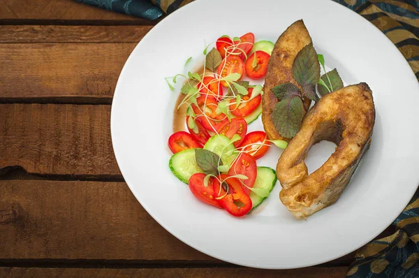 Gegrilltes Fischsteak mit Gemüse auf dem Teller: Tomaten, Microgran, Gurken, leckeres und gesundes Abendessen. rustikalen hölzernen Hintergrund. Ansicht von oben — Stockfoto