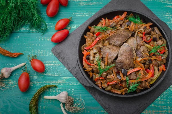 Foie de poulet frit avec des légumes et des herbes dans la poêle. Fond turquoise en bois. Vue du dessus — Photo