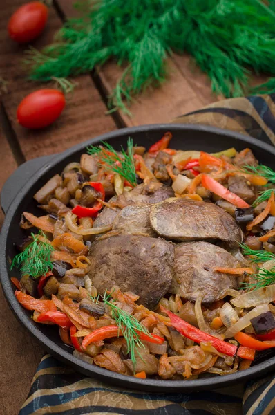 Fried chicken liver with vegetables and herbs in the frying pan. Wooden background. Top view