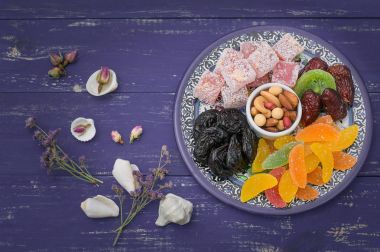 Doğu tatlılar kümesi. Marmelat, kivi, Kuru erik, rahat lokum, fındık, mandalina, Trabzon hurması, Kuru Kayısı, Kuru üzüm bir renkli mavi plaka Antep fıstığı, tarihler. Ahşap rustik arka plan. Üstten Görünüm