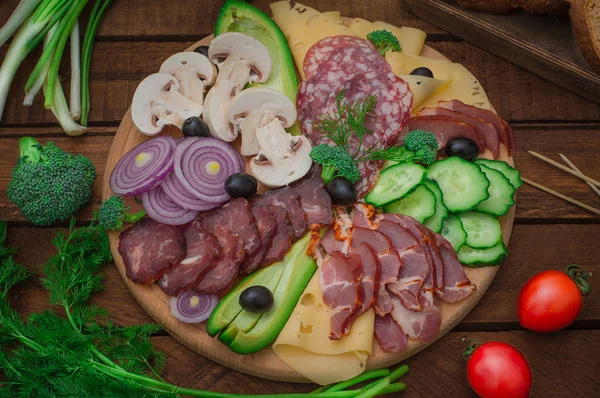 Kalt geräuchertes Fleisch mit Schinken, Salami, Speck, Schweinekoteletts, Käse, Pilzen, Gurken, Brot, Avocado, Zwiebeln und Oliven. rustikalen hölzernen Hintergrund. Ansicht von oben — Stockfoto