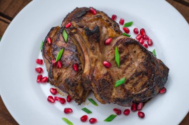 Narlı beyaz bir plaka üzerinde bir ızgarada pişmiş pirzola, biftek. Ahşap rustik arka plan. Üstten Görünüm