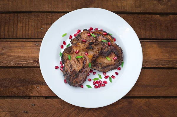 Steak auf Rippen, gegrillt mit Granatapfel auf einem weißen Teller. rustikalen hölzernen Hintergrund. Ansicht von oben — Stockfoto