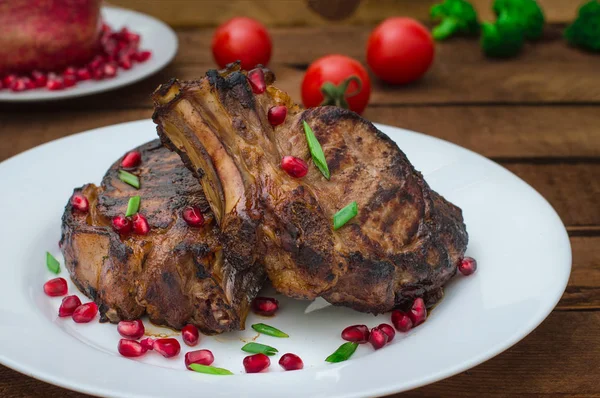 Narlı beyaz bir plaka üzerinde bir ızgarada pişmiş pirzola, biftek. Ahşap rustik arka plan. Üstten Görünüm