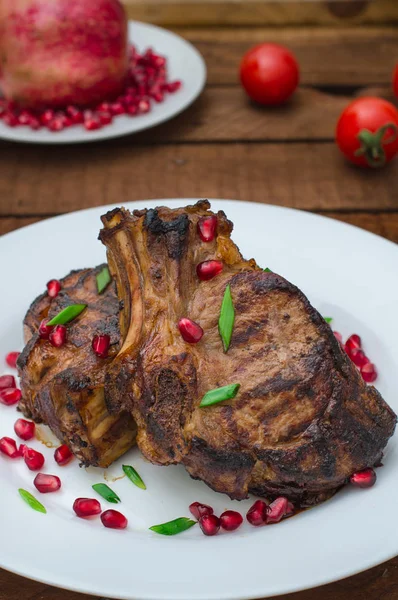 Narlı beyaz bir plaka üzerinde bir ızgarada pişmiş pirzola, biftek. Ahşap rustik arka plan. Üstten Görünüm