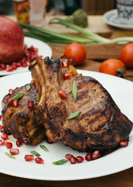 Steak na žebra, vařené na grilu s granátovým jablkem na bílé plotně. Dřevěný rustikální pozadí. Pohled shora — Stock fotografie