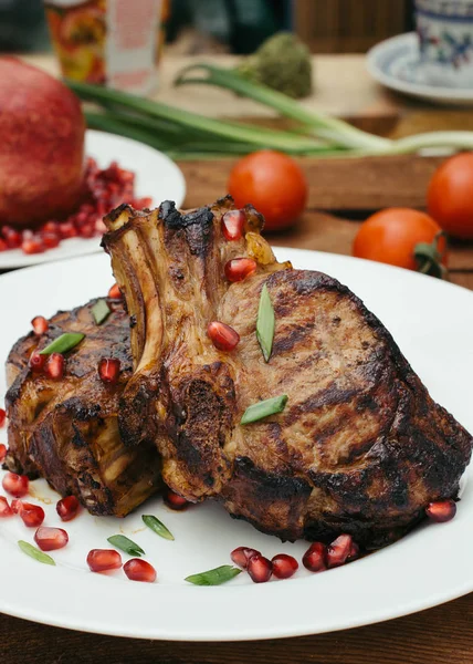 Steak sur côtes levées, cuit sur un gril avec grenade sur une assiette blanche. Fond rustique en bois. Vue du dessus — Photo